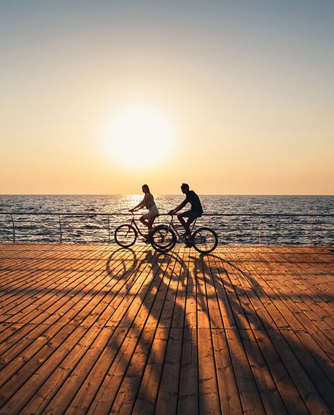 Couple of young hipsters cycling together at the beach at sunrise sky at wooden deck summer time